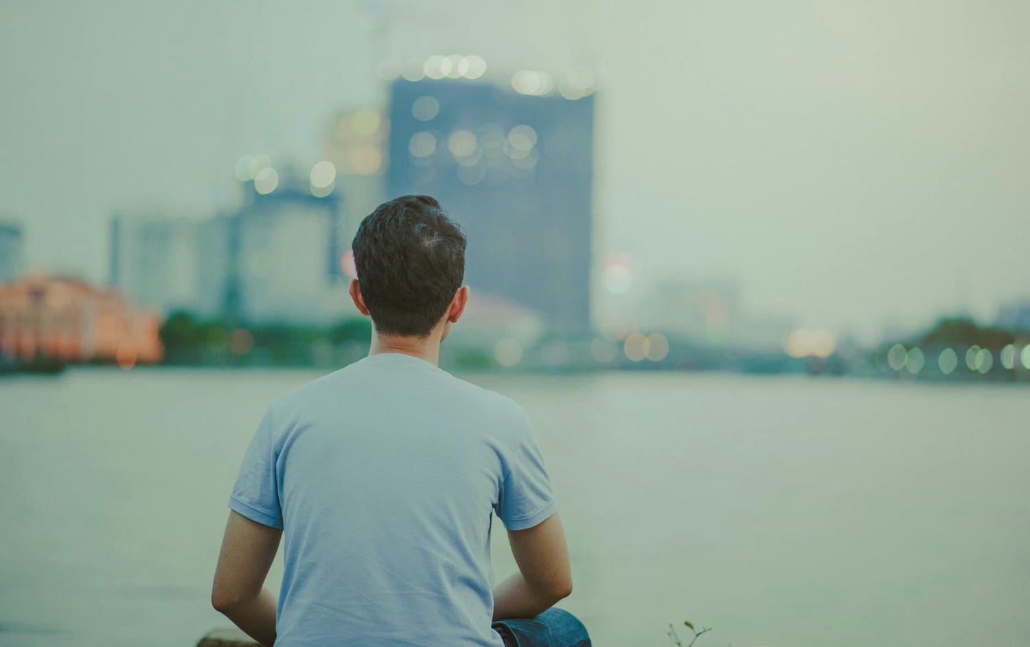 photo of man wearing blue shirt sitting looking on high rise buildings