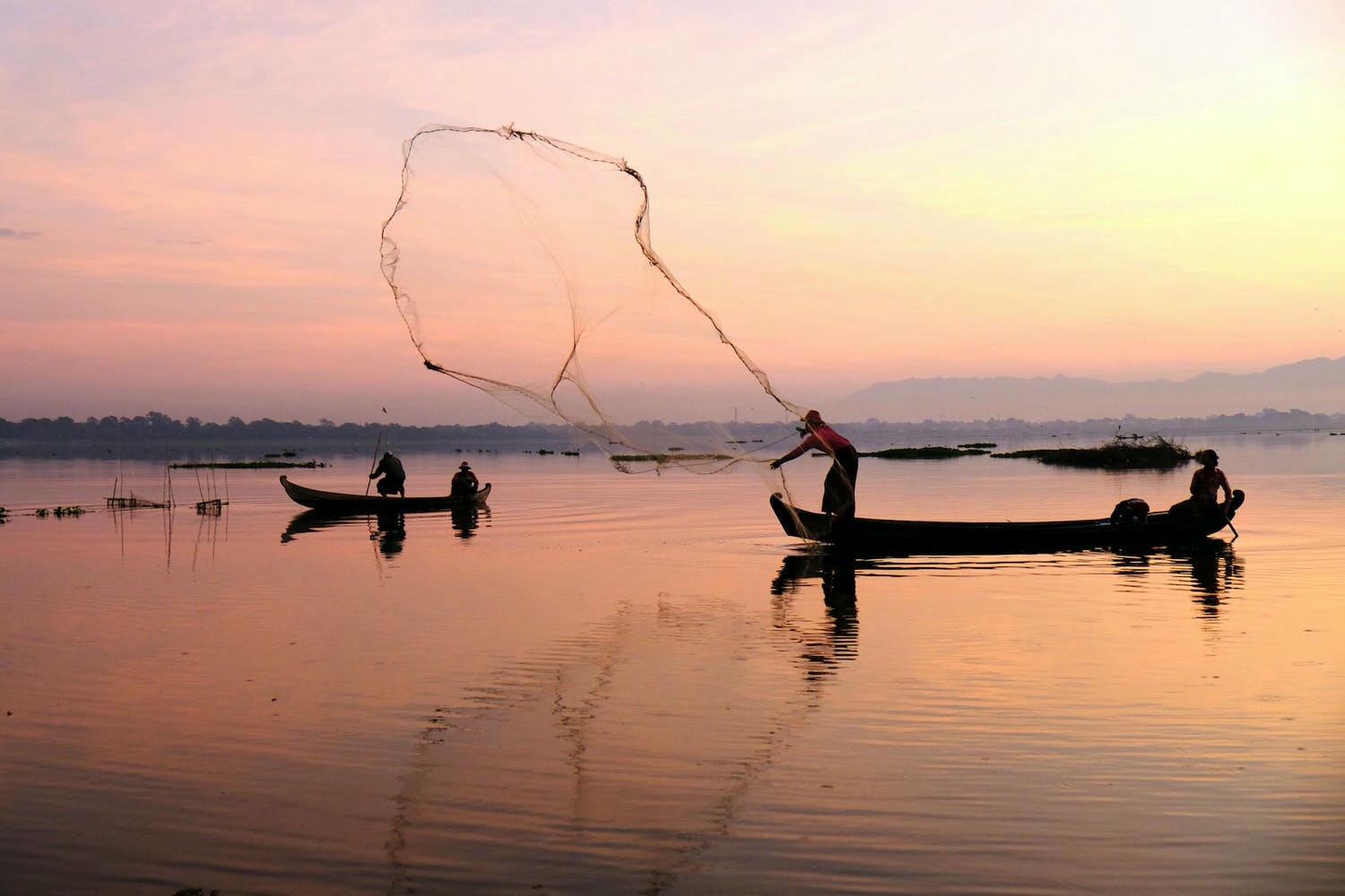 fisherman throwing net into body of water